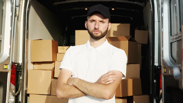 a male mover stands in front of a delivery car